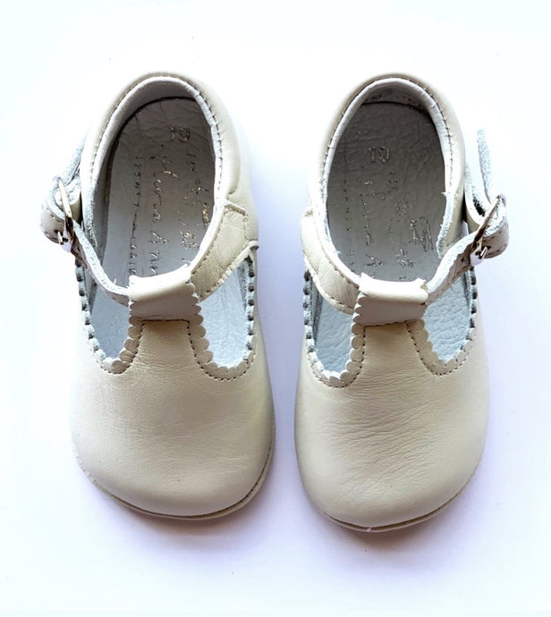 Cream leather T-Bay UNISEX shoe for baby and toddlers, made in a traditional style and pretty scalloped edge. They have a T bar strap with adjustable buckle strap. Ideal for any day occasion, parties, baptism etc.